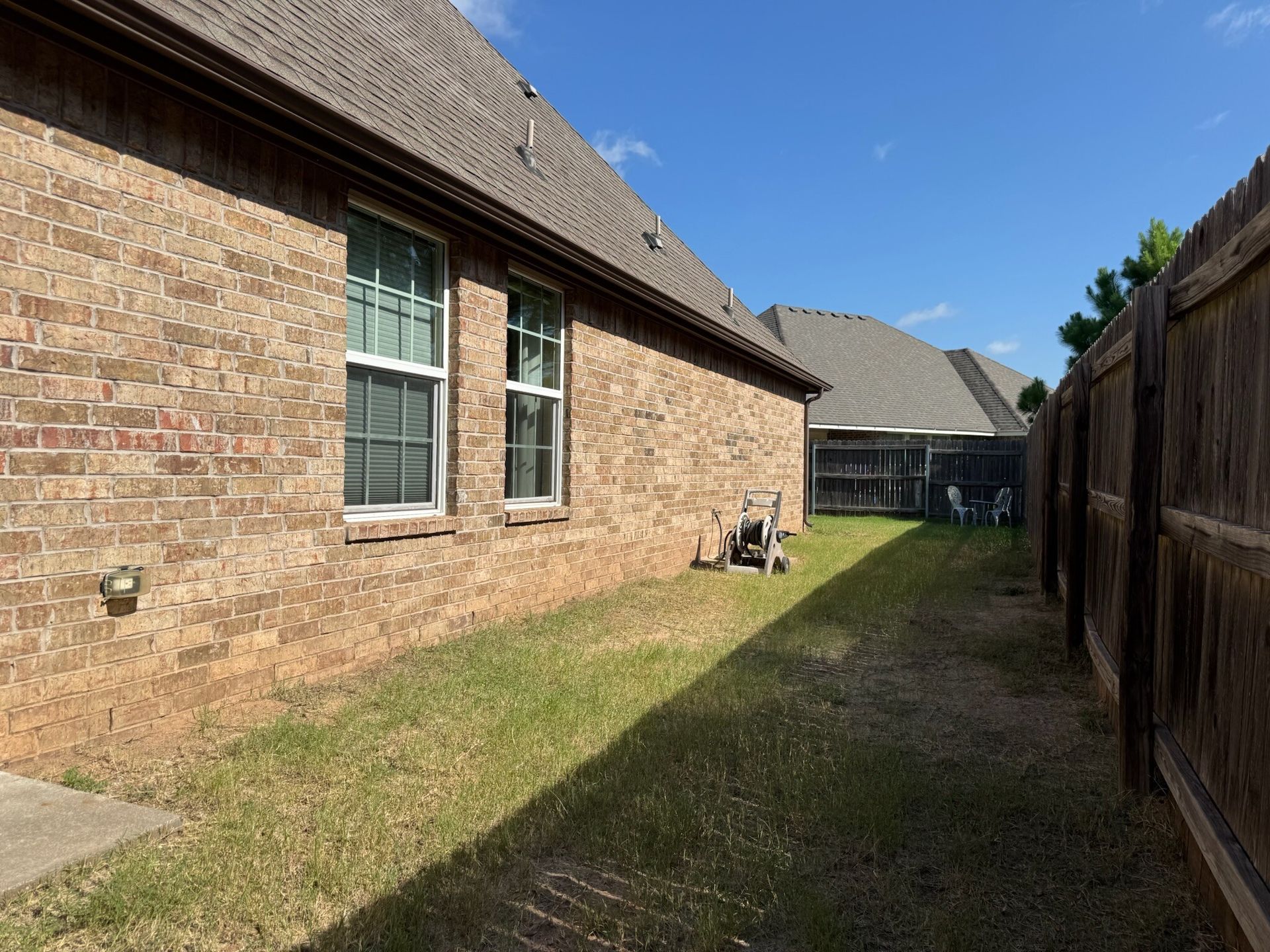 Side view of a brick house with windows, a small lawn, and a wooden fence on a sunny day.