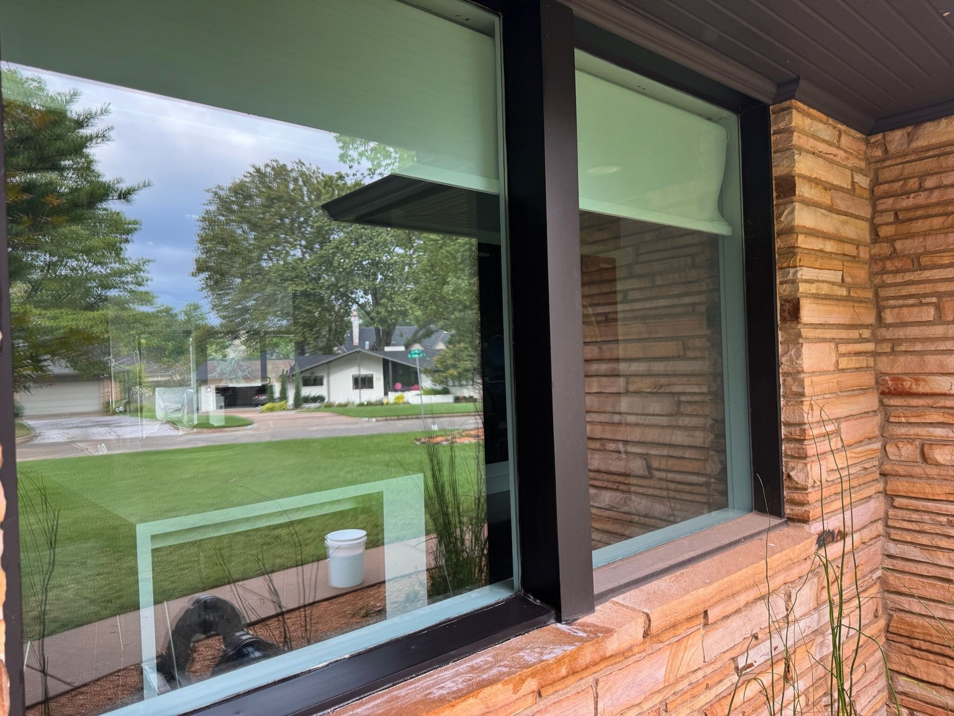 Exterior window with black frame, reflecting a green lawn, house, and cloudy sky.