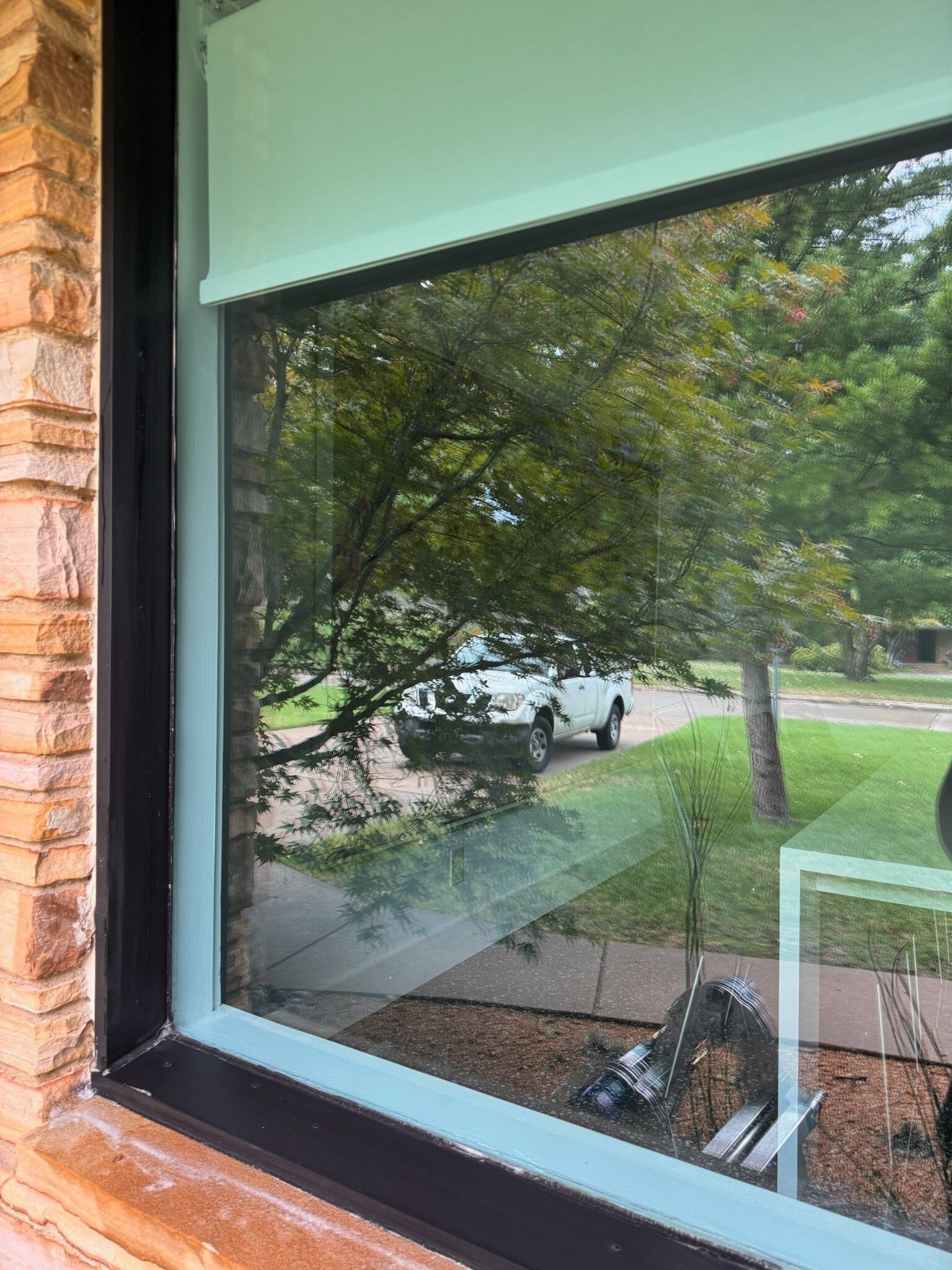 View through a window with a green frame, reflecting a street scene with a vehicle and trees.