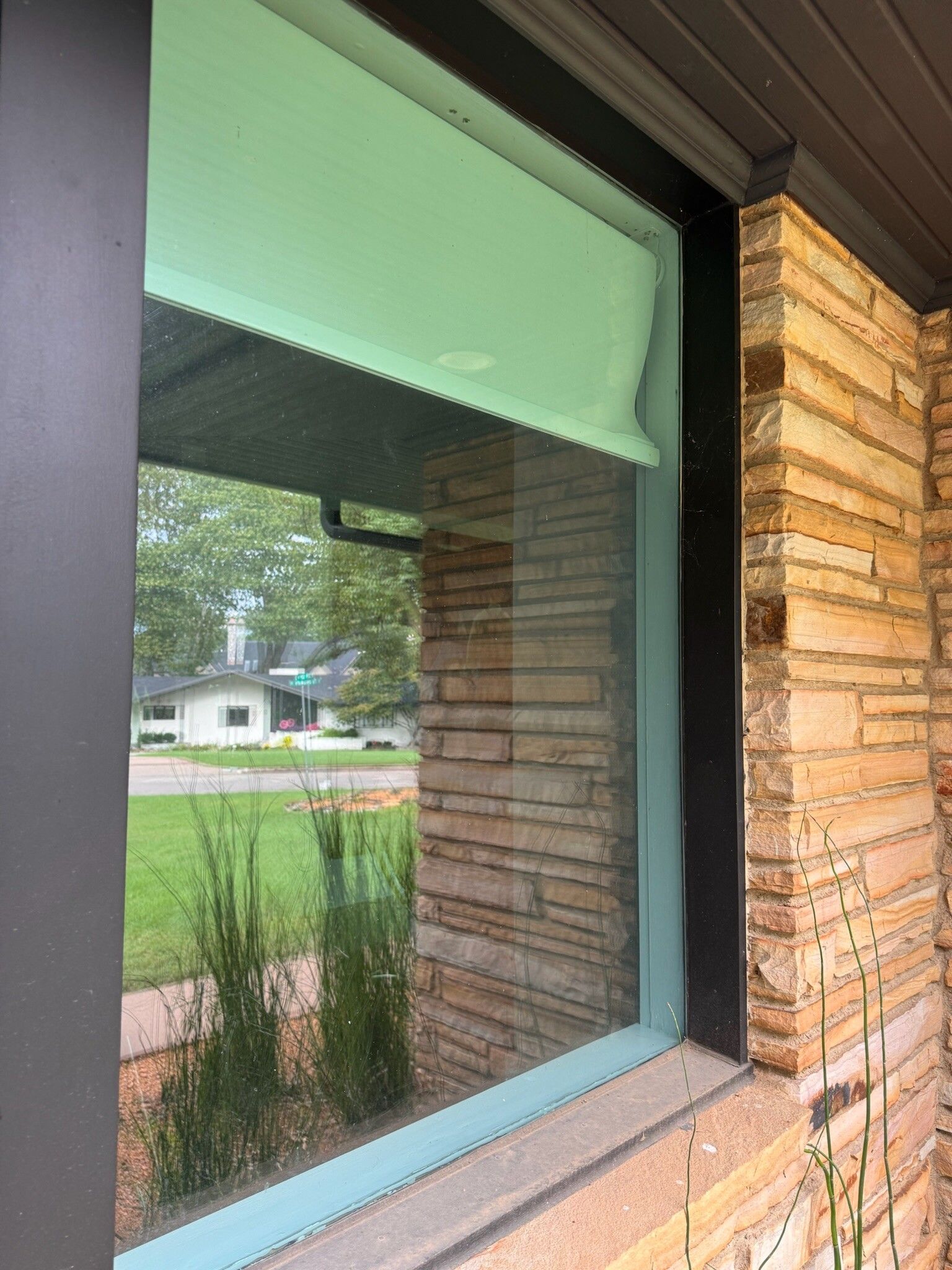 Window frame with brick wall and green lawn visible through the glass.