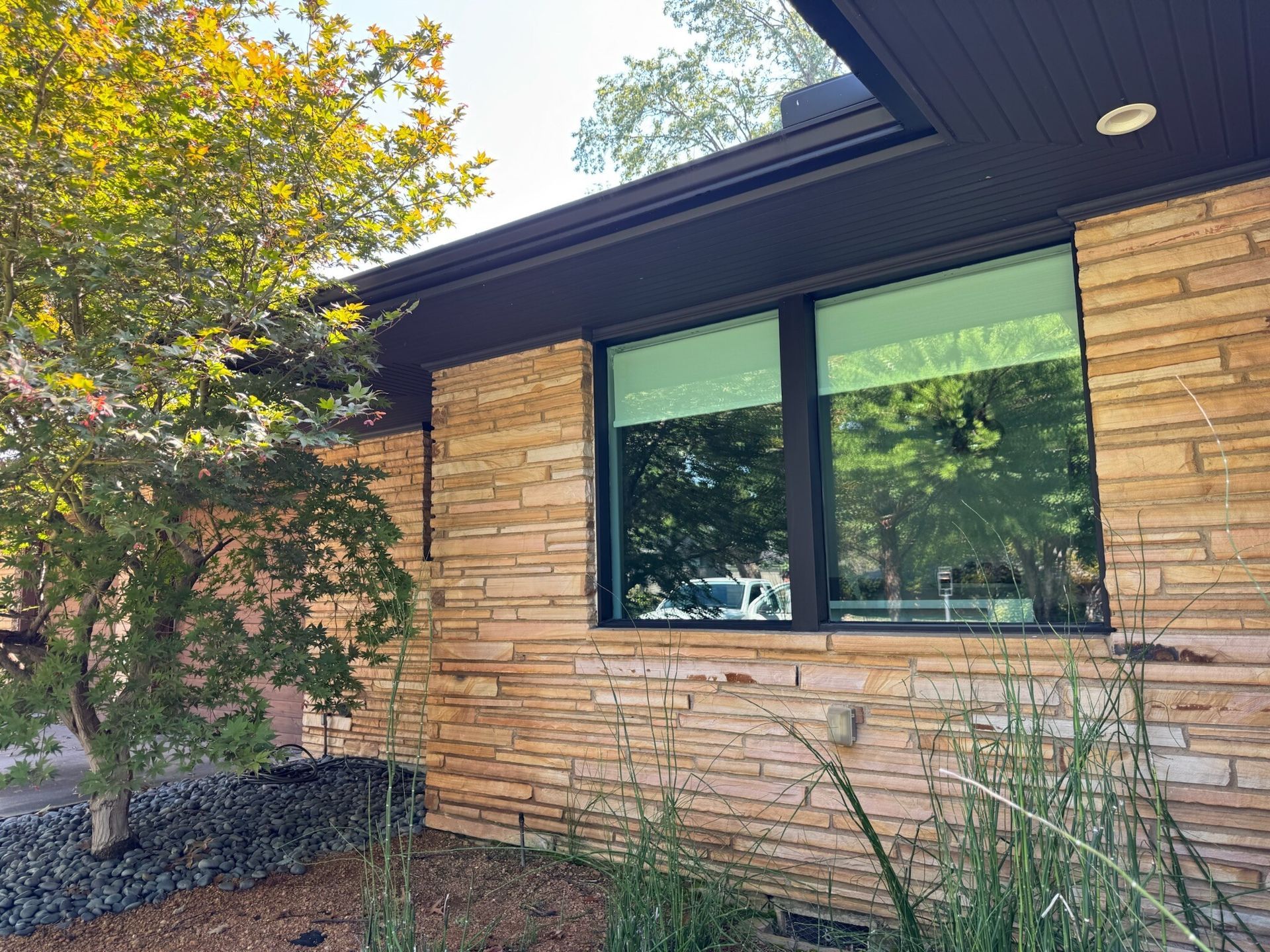 Exterior view of a house with stone siding, a dark trim, and a window reflecting trees.