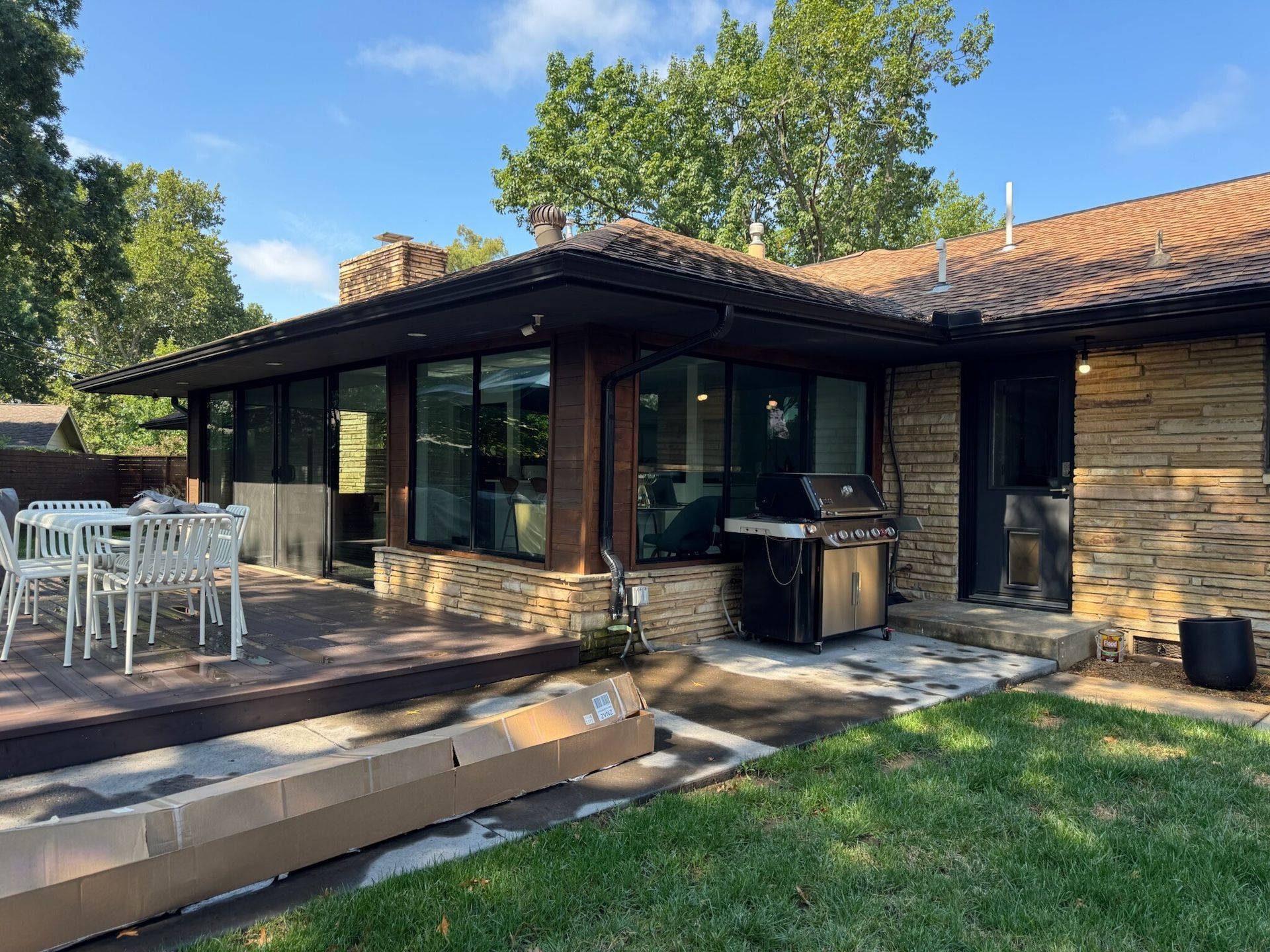 Backyard patio with deck, grill, and glass windows under a tiled roof.