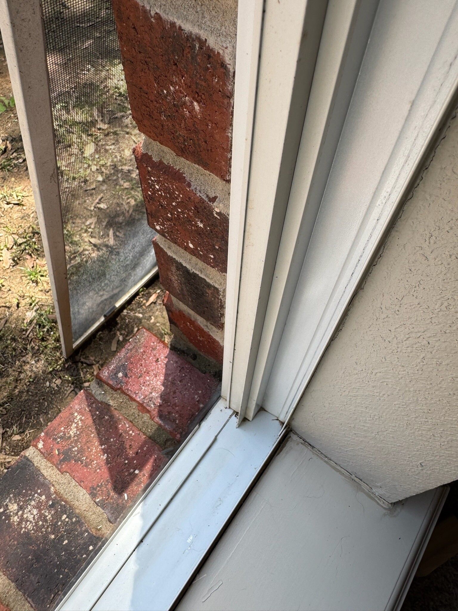 Close-up of a white window frame and sill against red brick, with a screen visible.