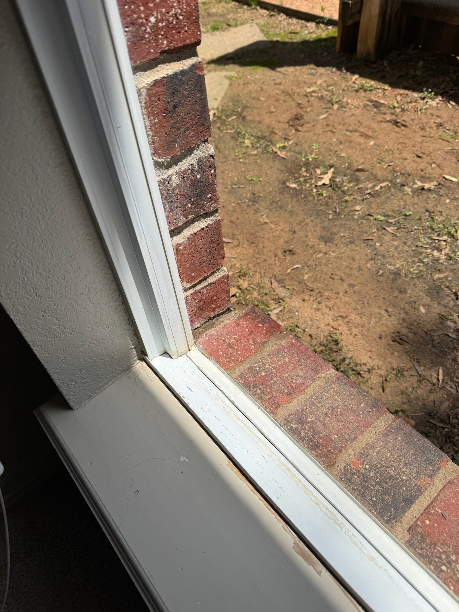 White window frame next to red brick wall. Outside view of dirt and some grass.