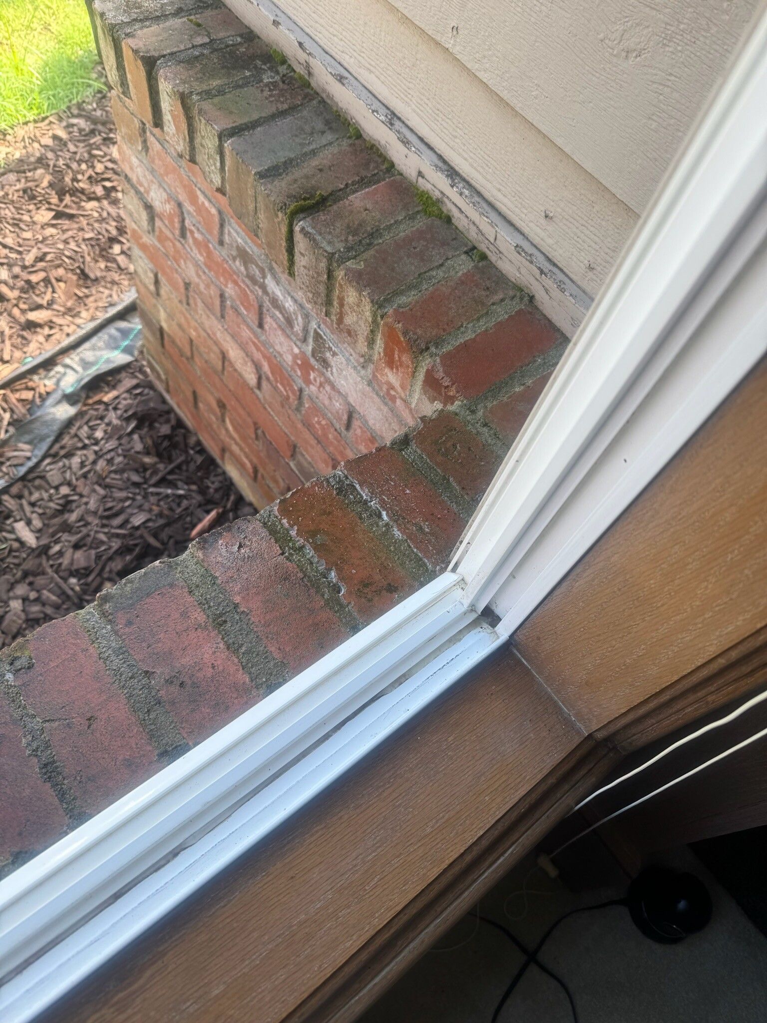 Window frame against a brick wall with visible moss. Brown wooden sill is also visible.