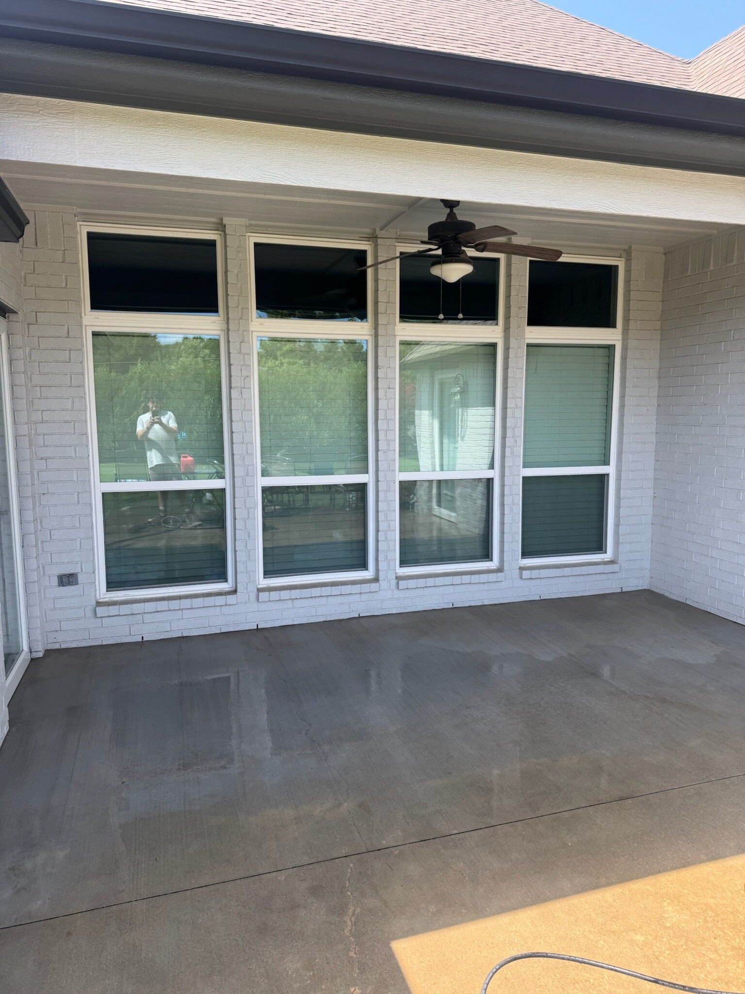 Exterior patio with windows, gray brick wall, and a ceiling fan.