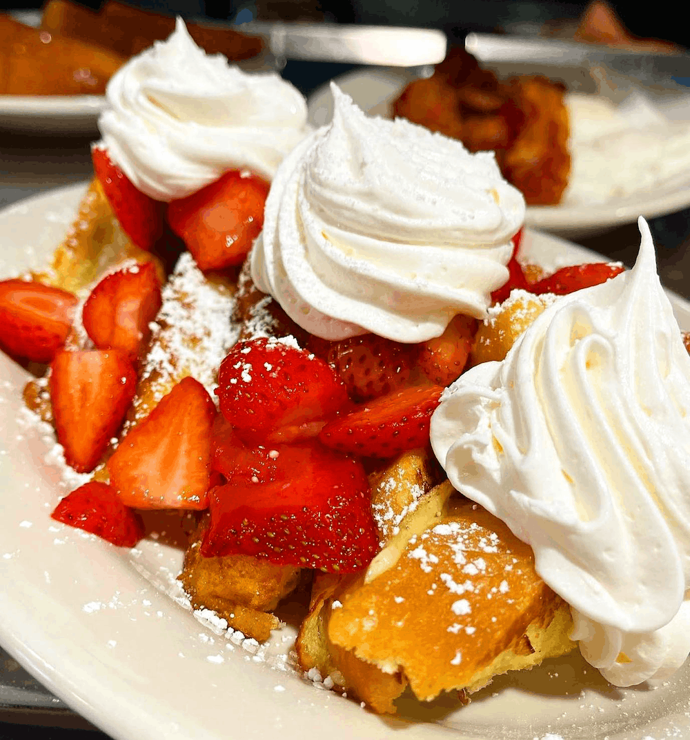 French toast with strawberries and whipped cream on a plate.