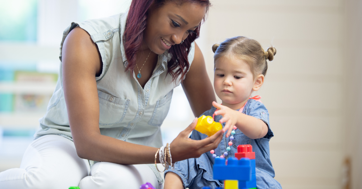 A woman is playing with a little girl who is sitting on the floor.