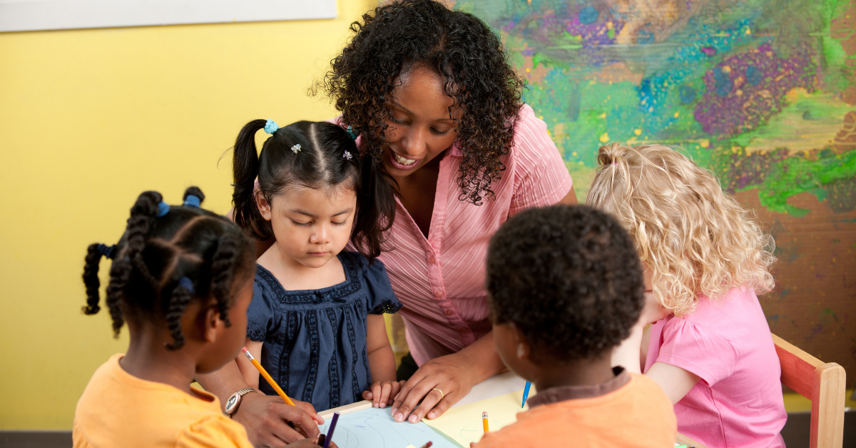 A group of children are sitting around a table with a teacher.