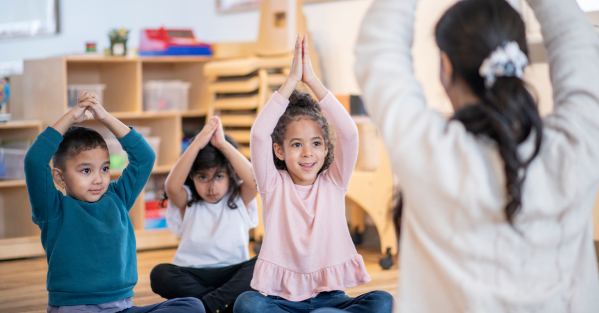 A group of children are doing yoga together in a classroom.