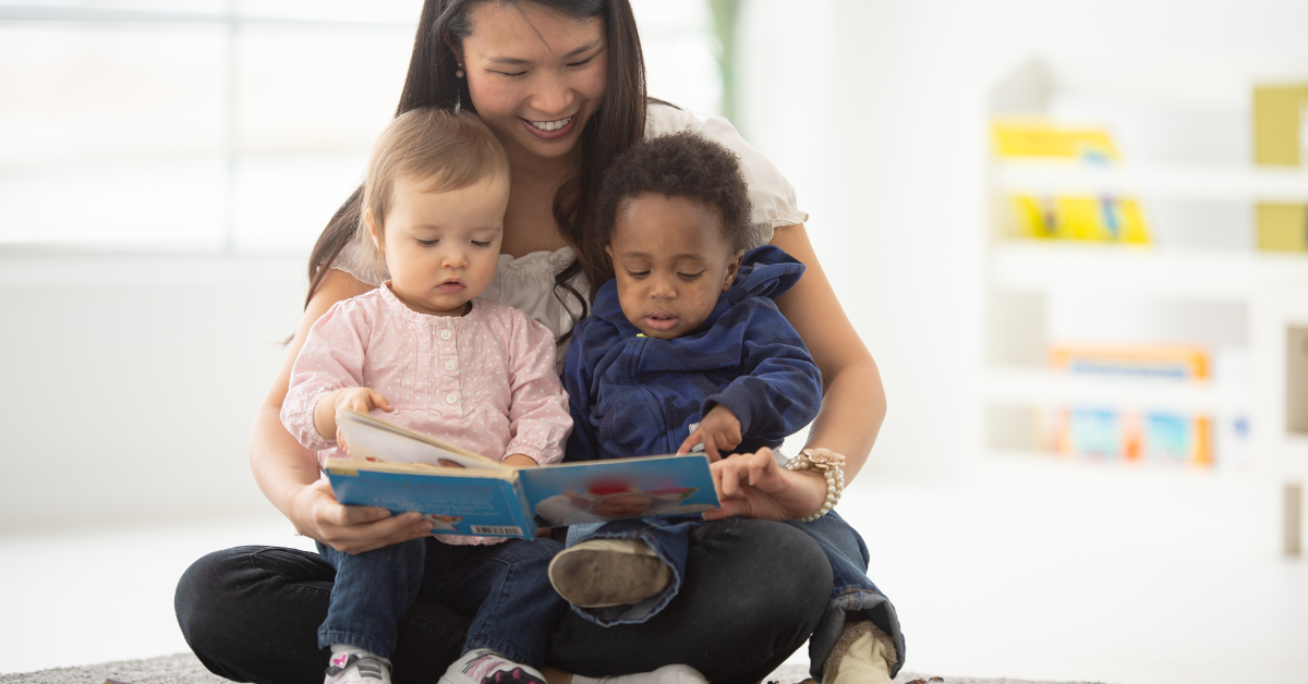 A woman is sitting on the floor reading a book to two babies.