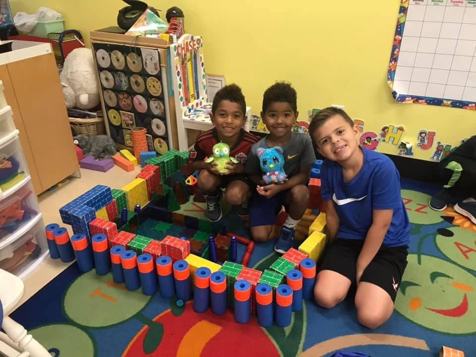 Three young boys are sitting on the floor playing with toys.