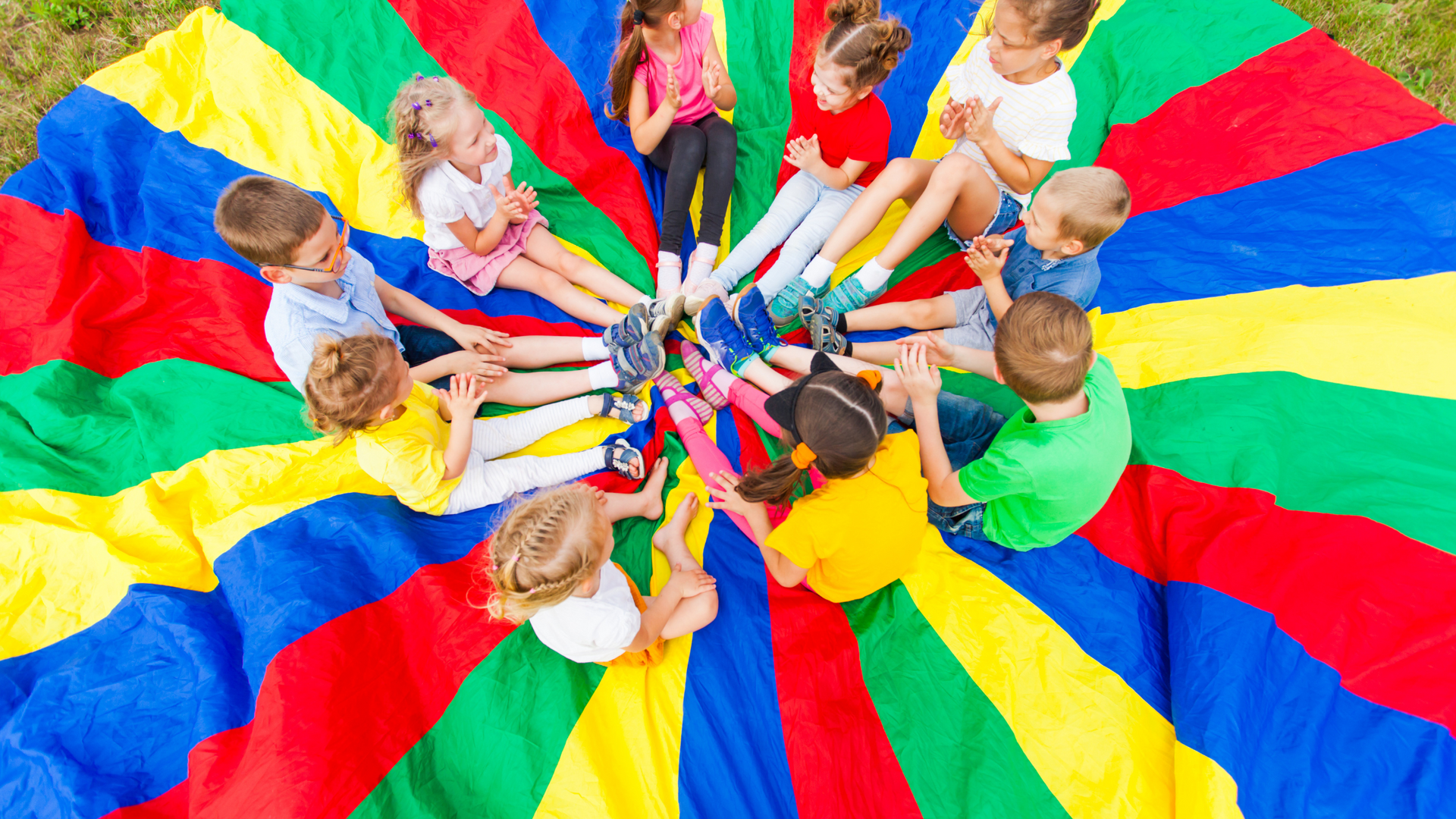 A group of children are sitting in a circle on a colorful parachute.