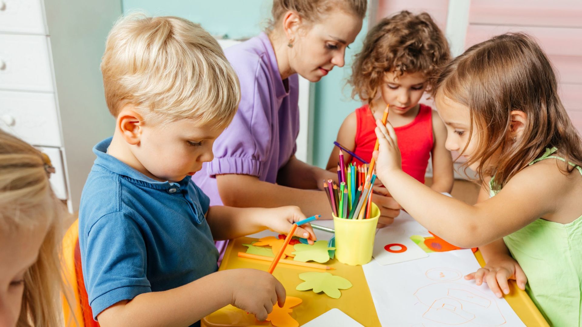 Children and an adult at a table doing crafts; drawing, high-fiving.