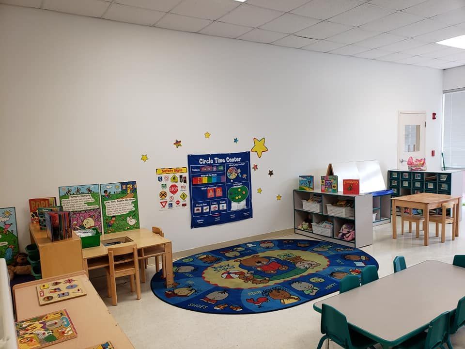 A classroom with tables and chairs and a rug on the floor.