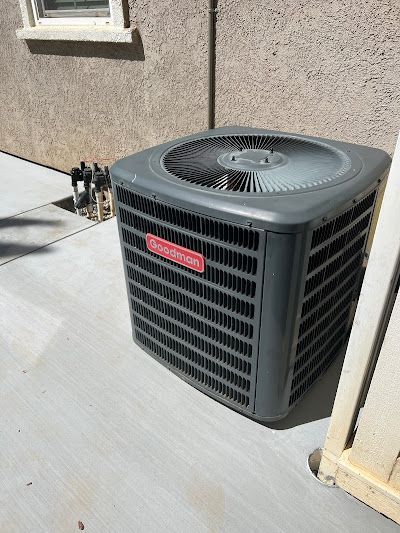 A gray air conditioner is sitting on the sidewalk in front of a building.