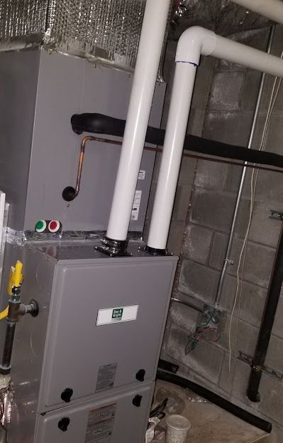 A furnace is sitting in a basement next to pipes.