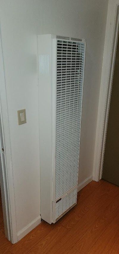 A white heater is sitting in a corner of a room next to a door.