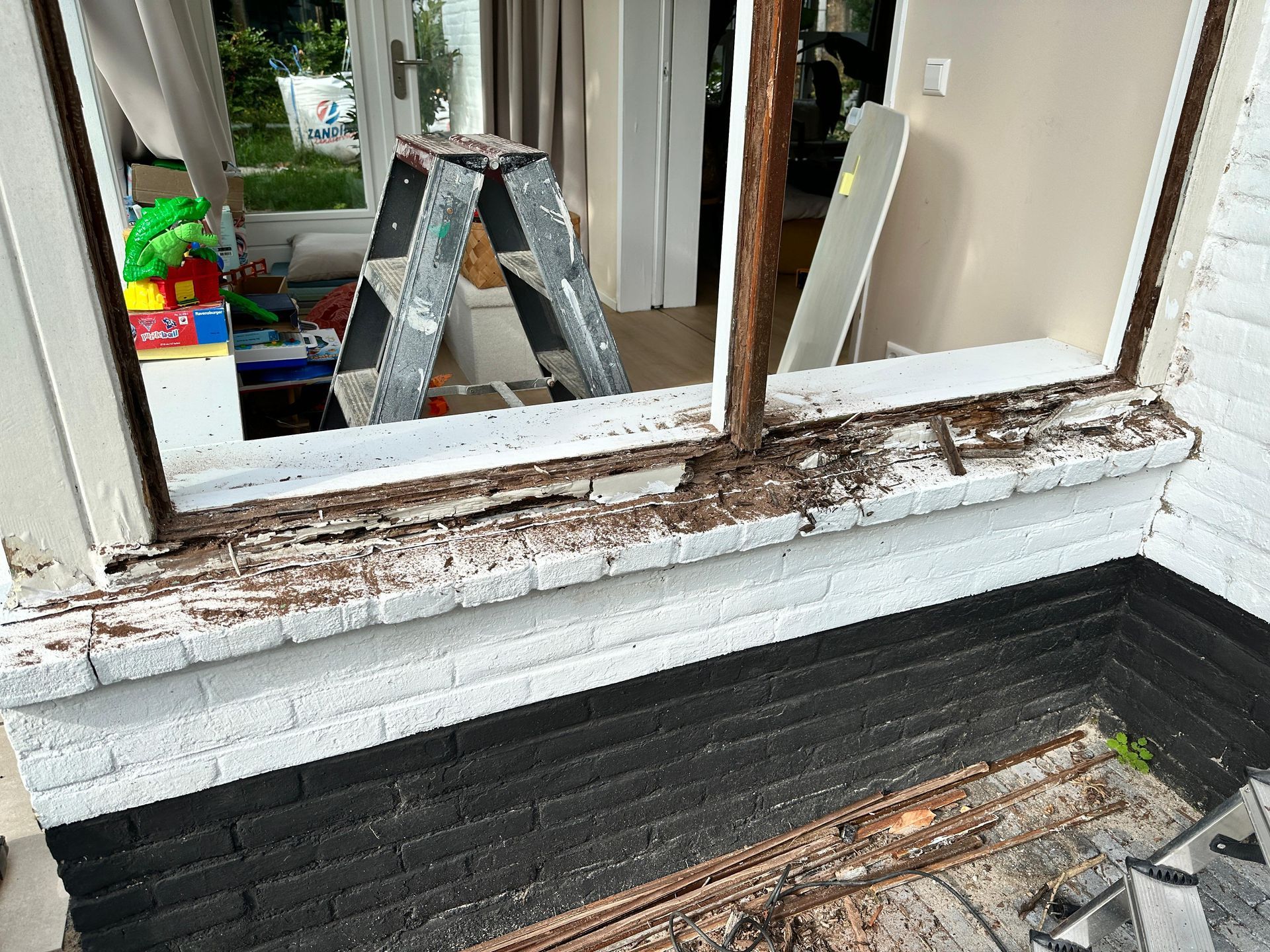 Er staat een ladder voor een raam dat beschadigd is door termieten.
