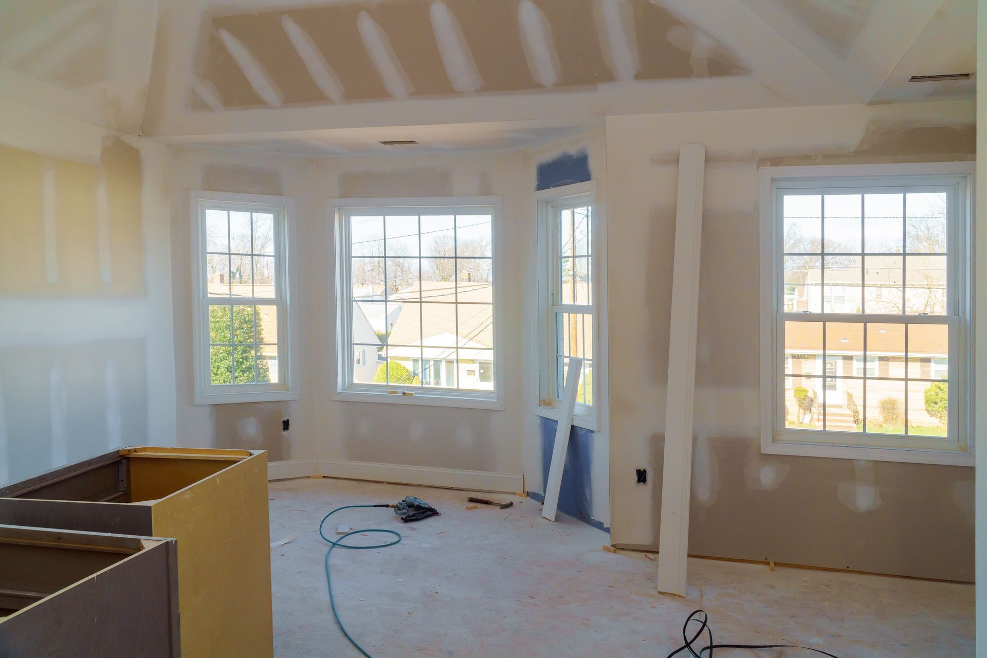 Unfinished living room with large windows, exposed beams, and construction materials on the floor.