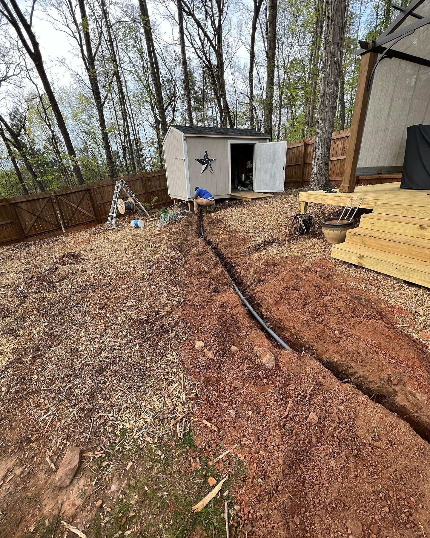 A shed is sitting in the middle of a dirt field next to a wooden deck.