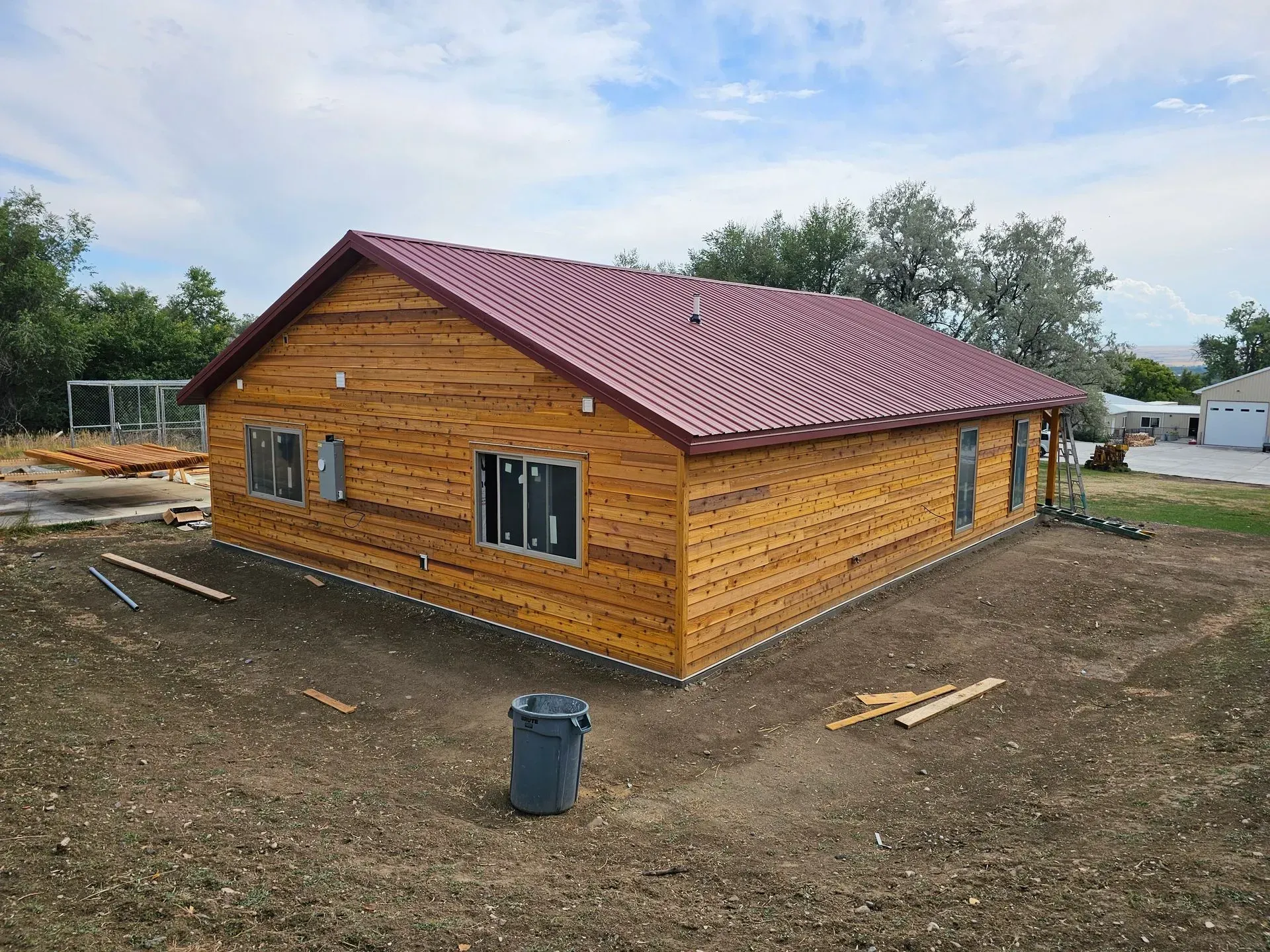 A large wooden house with a red roof is being built in a dirt field.