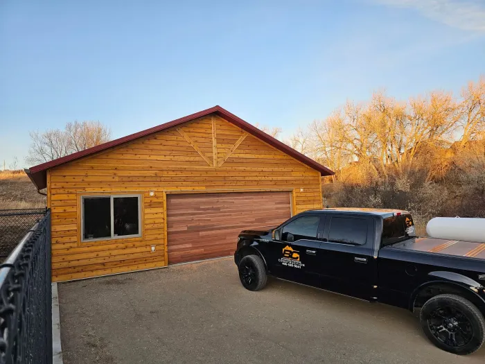 A black truck is parked in front of a wooden garage.