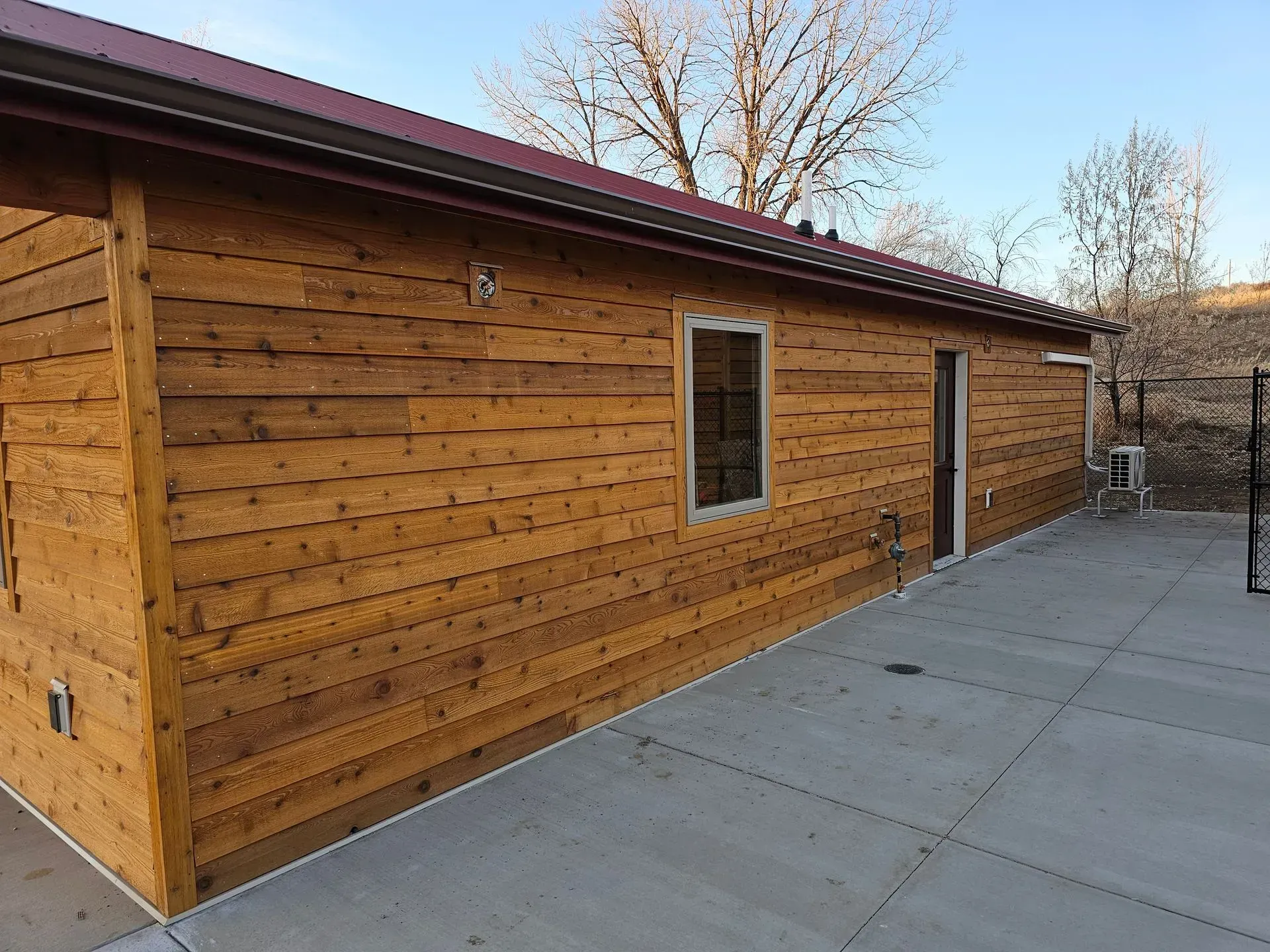 A wooden building with a red roof and a concrete patio in front of it.