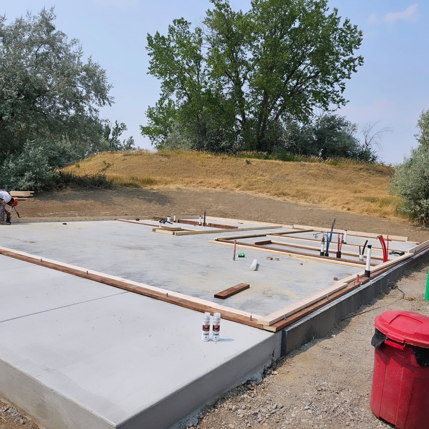 A red trash can sits next to a concrete foundation
