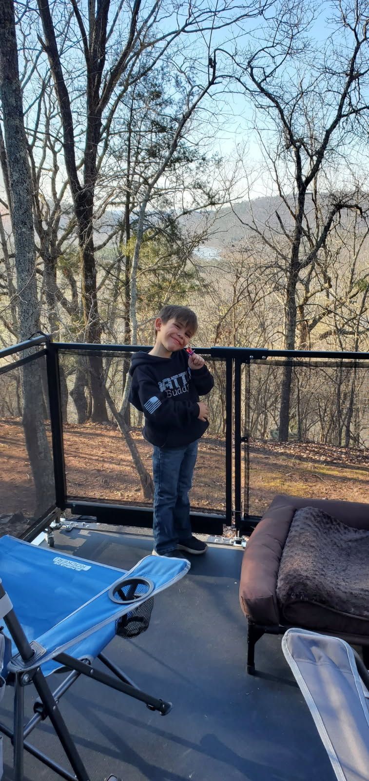A young boy is standing on a balcony overlooking a forest.