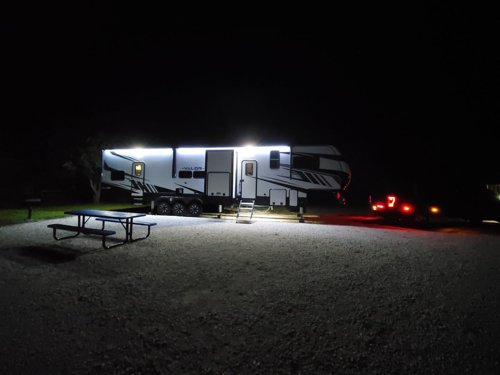 A rv is parked in a gravel lot at night