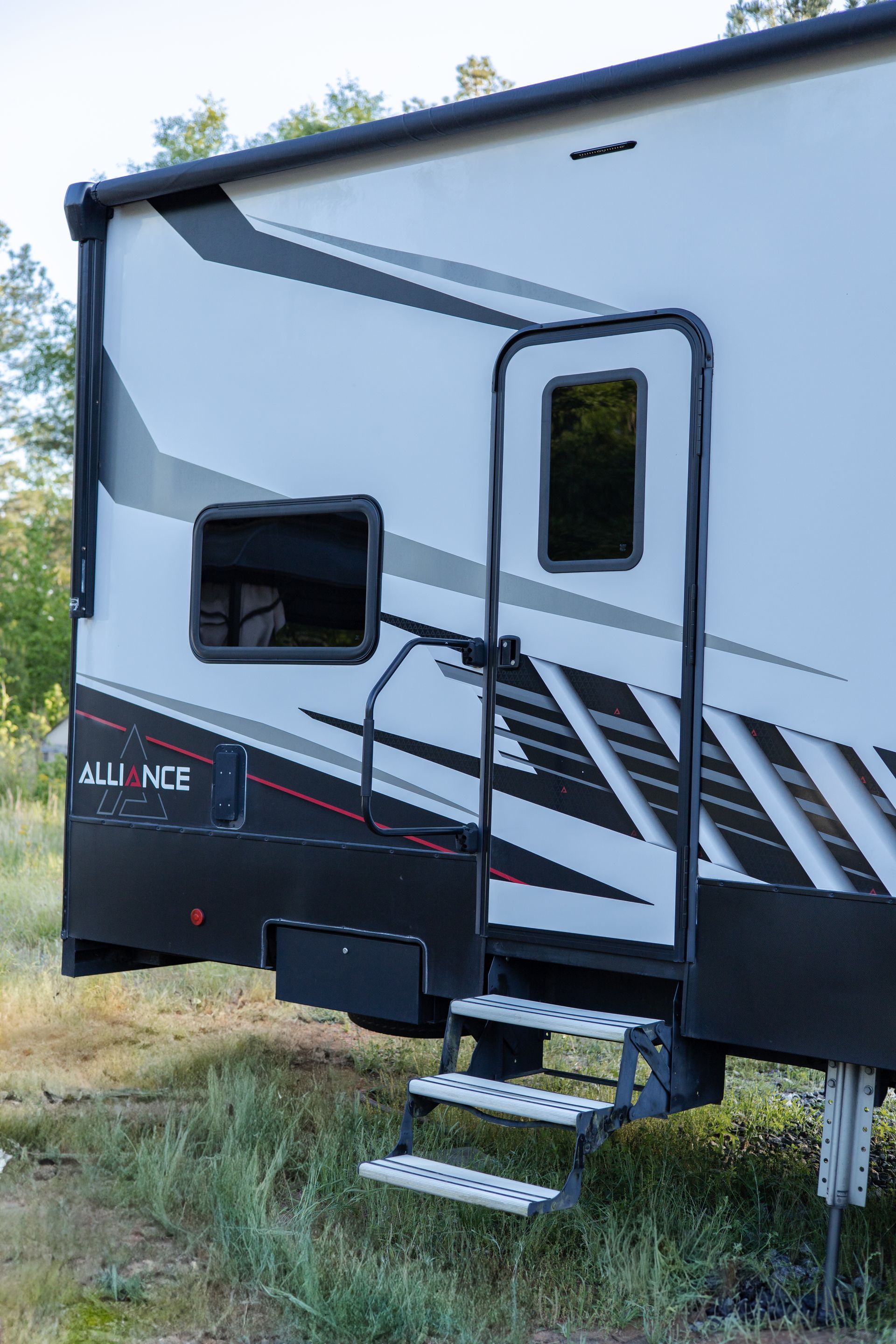 A white and black trailer with stairs leading up to it is parked in a field.