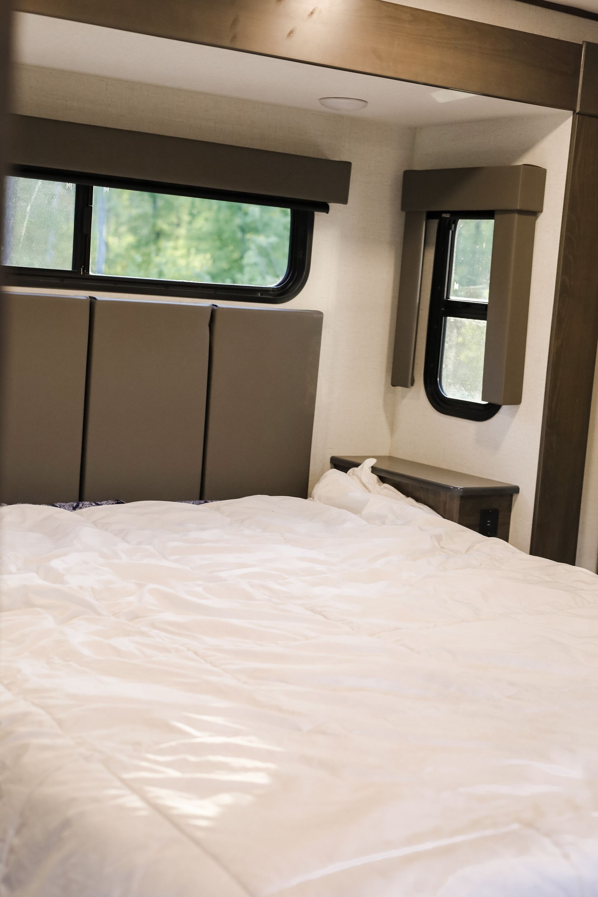 A bedroom in a rv with a bed and two windows.