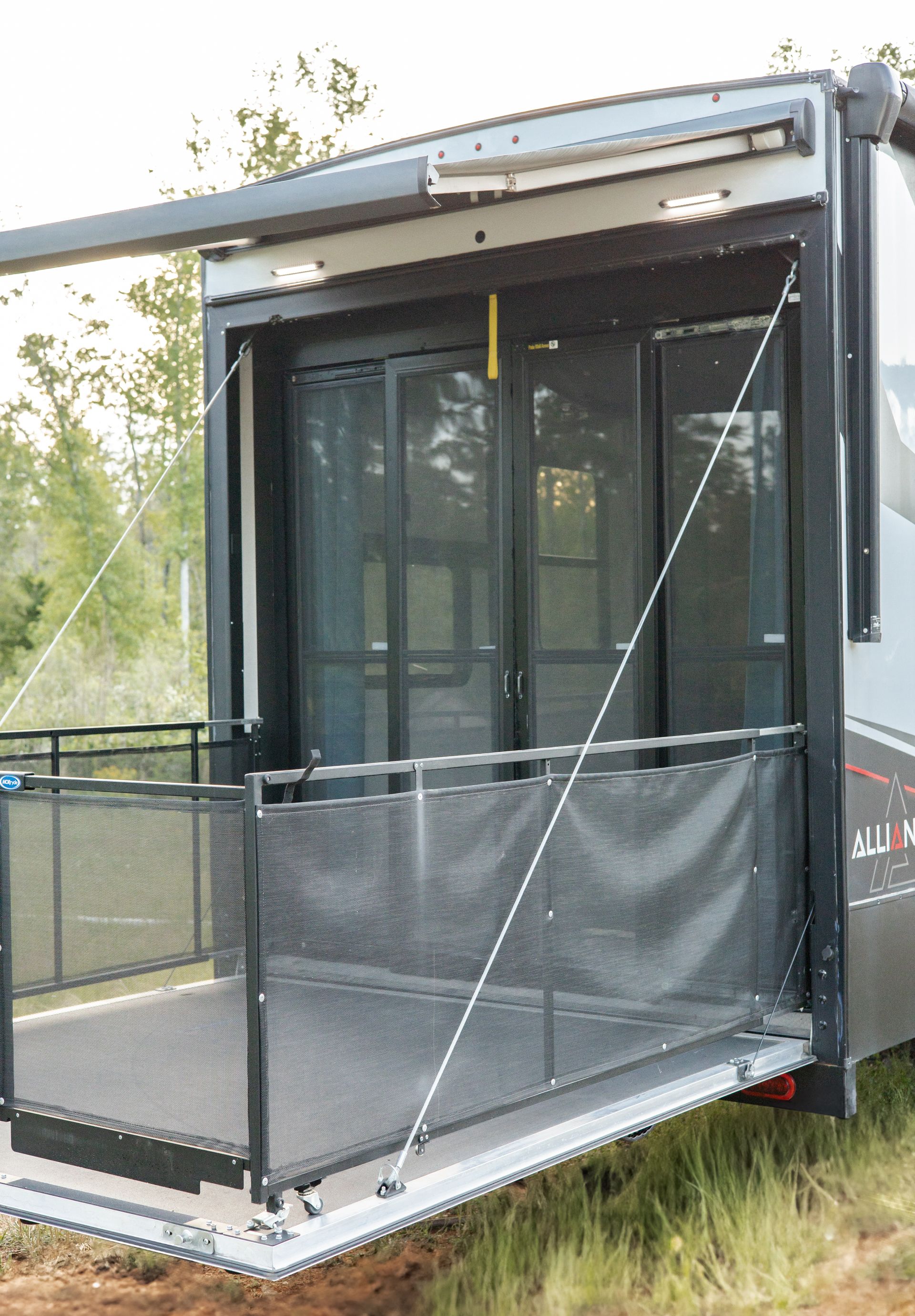A trailer with a balcony and sliding glass doors is parked in the grass.