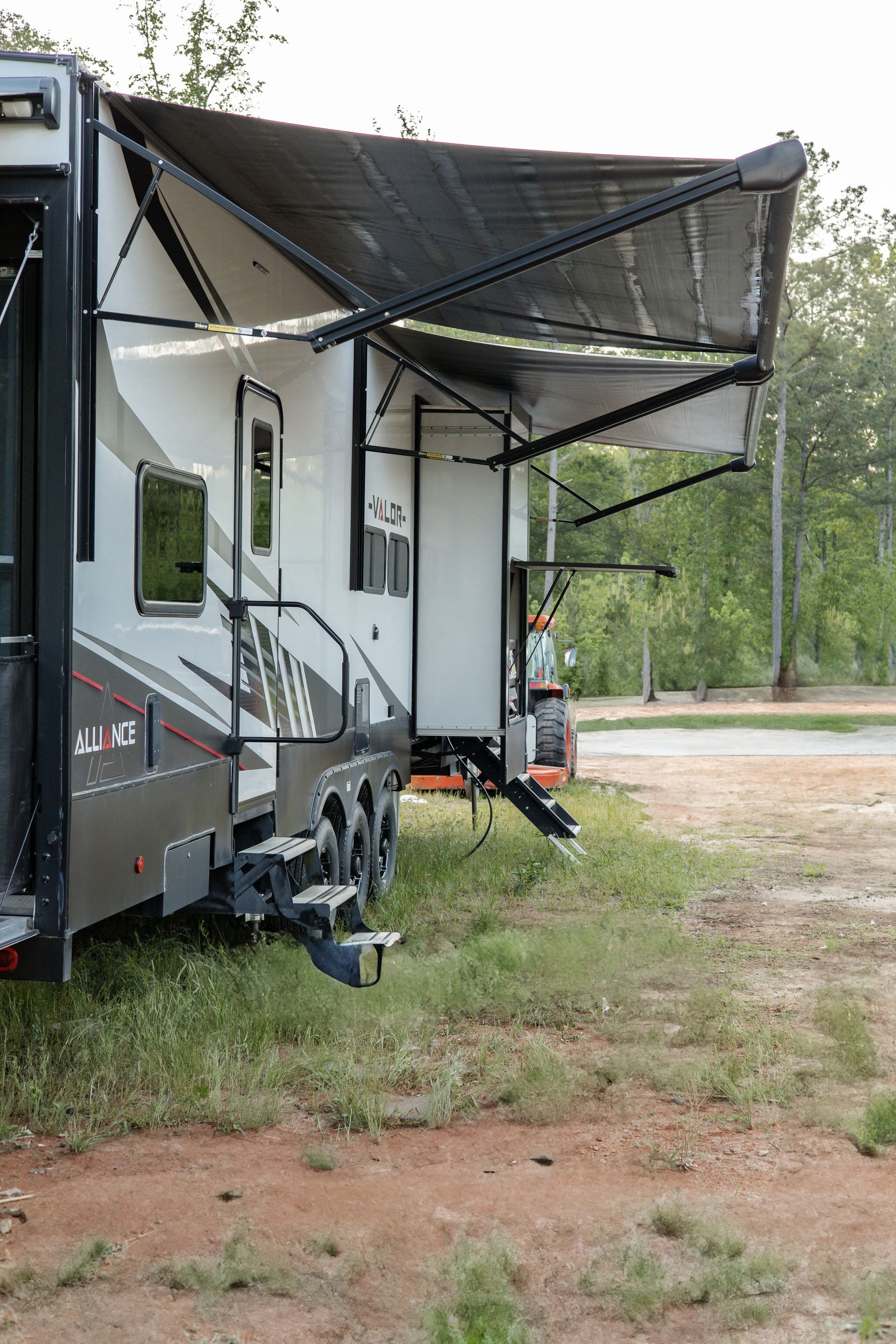 A rv with an awning is parked in a grassy field.