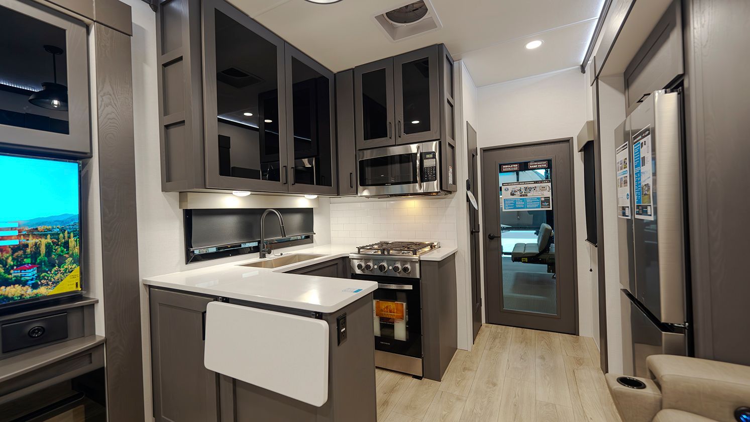 A kitchen in a rv with a stove , refrigerator , microwave and television.