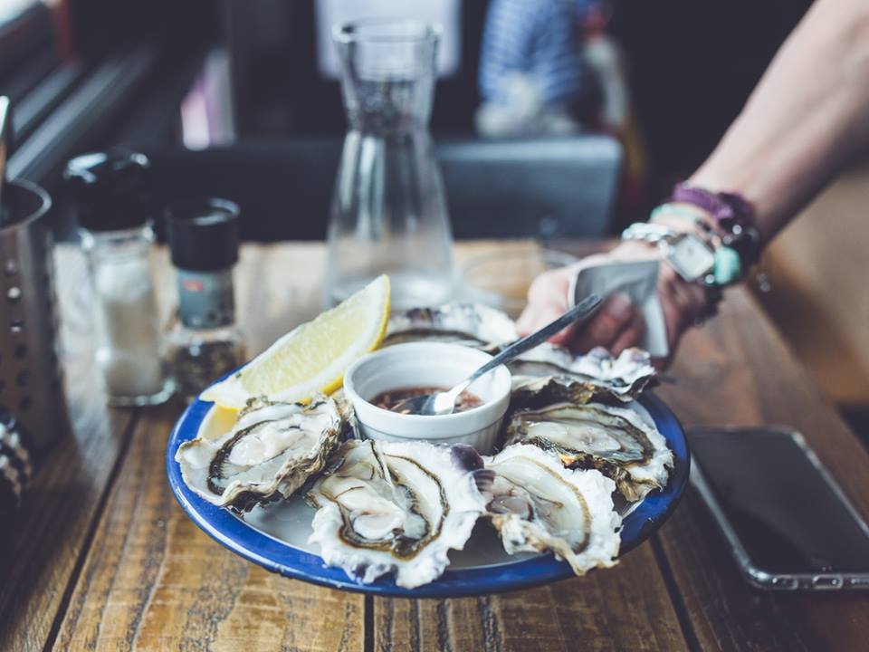 A person is holding a plate of oysters on a wooden table.