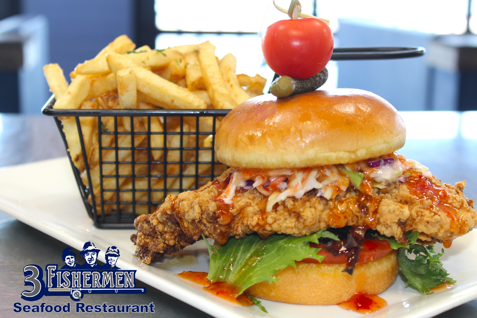 A fried chicken sandwich with a basket of french fries on a white plate