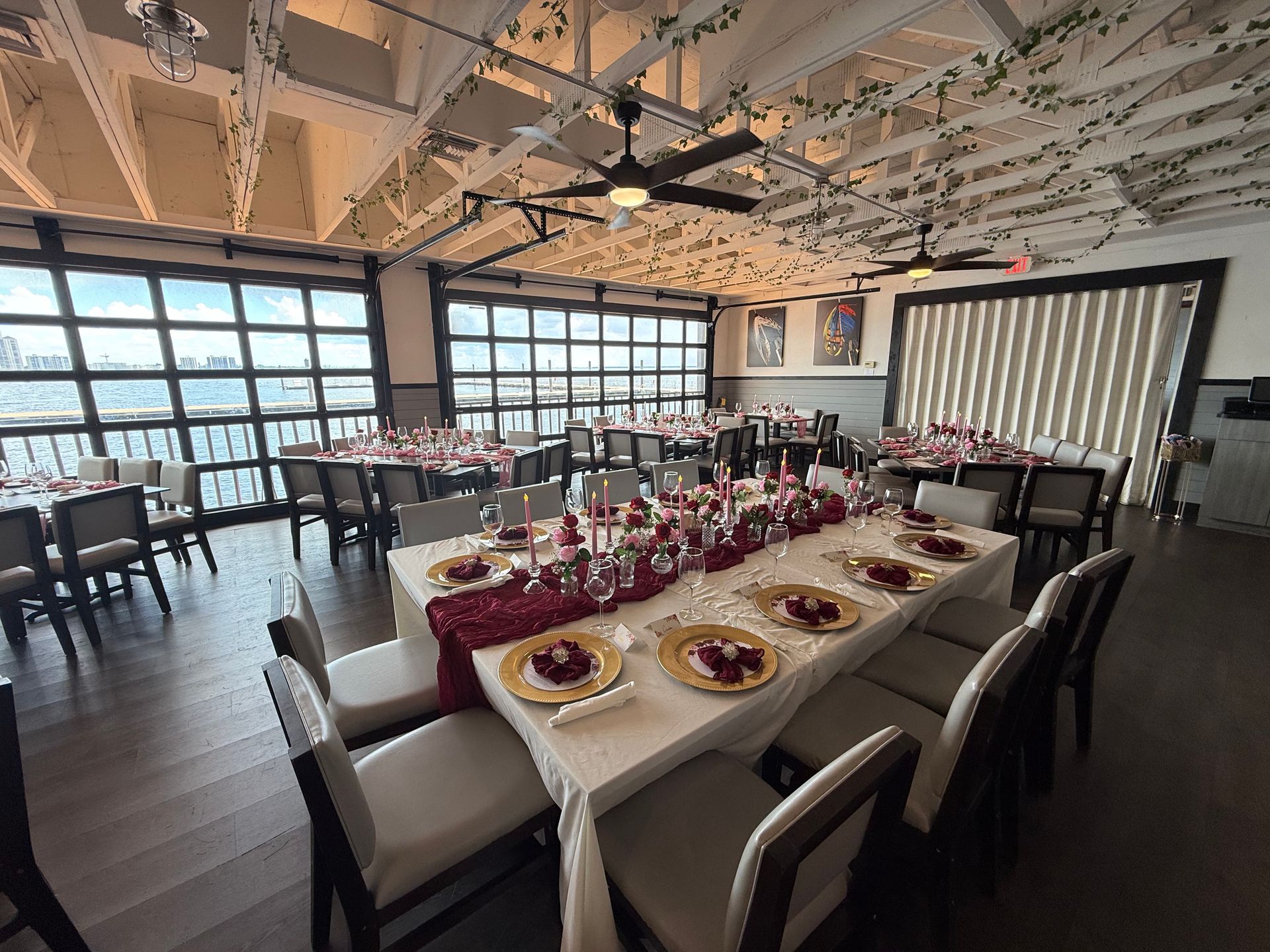 Restaurant dining room set for a celebration. Tables are decorated with red and gold, overlooking a waterfront view.