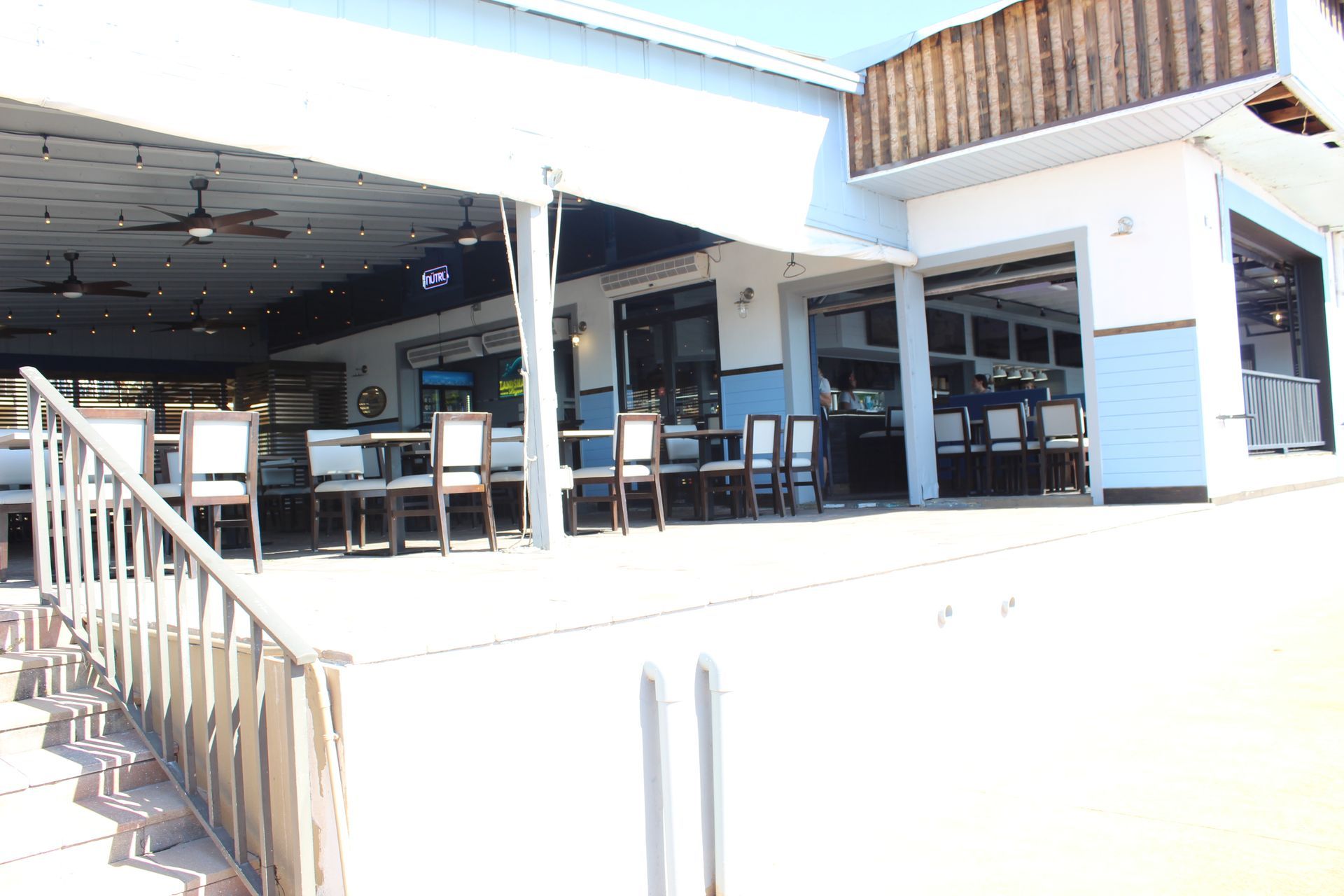 A restaurant with tables and chairs outside and stairs leading up to it