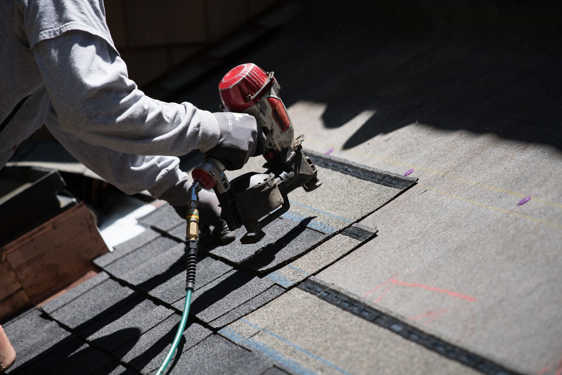 Roofer using a nail gun to secure shingles during roof repair.