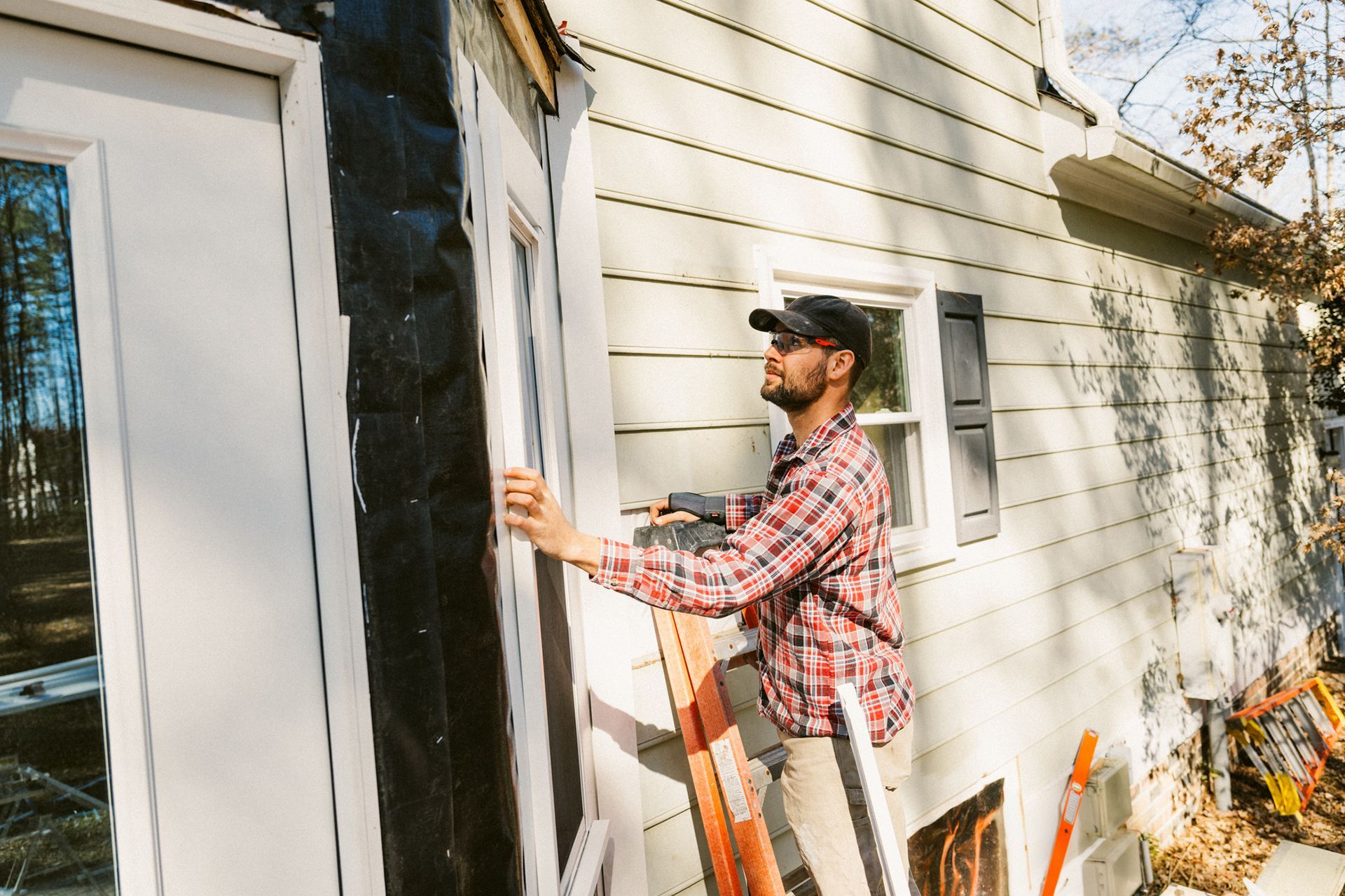 A man working on residential siding installation, attaching panels to the exterior of a house.