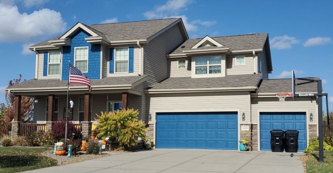 A large house with blue garage doors and an american flag on the front porch.