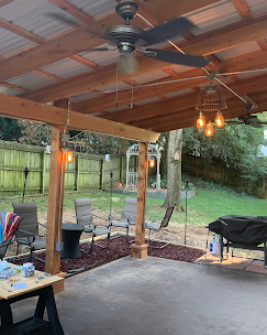 Patio with overhead wooden frame, string lights, ceiling fans, and outdoor furniture in a backyard.