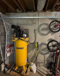 Yellow DeWalt air compressor in a basement, with a hanging hose and bikes on the wall.