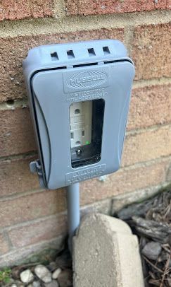 Gray weatherproof electrical outlet cover on a brick wall, protecting an outlet.