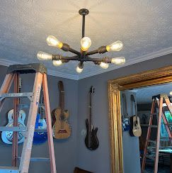 Ceiling light with Edison bulbs, next to guitars on a gray wall. Two ladders in the frame.