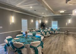 Formal event hall with round tables set for a party, teal and white decor, light gray walls, wood floors.