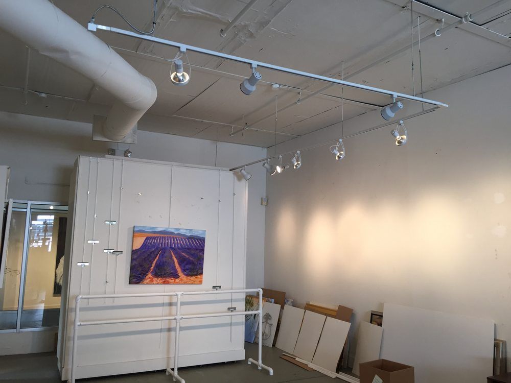Empty art gallery with track lighting illuminating a painting. White walls and a white support structure.