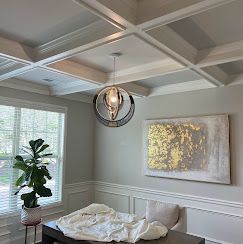Dining room with coffered ceiling, chandelier, art, and table covered with fabric.